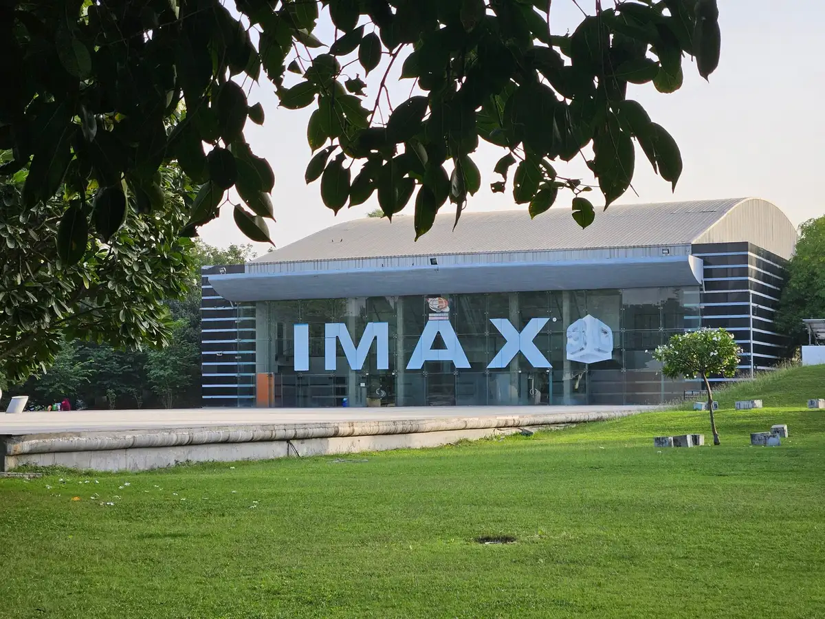 A stack of IMAX 70mm film reels on a projection room shelf, each reel weighing roughly 600 pounds, the film leader visible, dramatic shadows cast by projection booth lighting