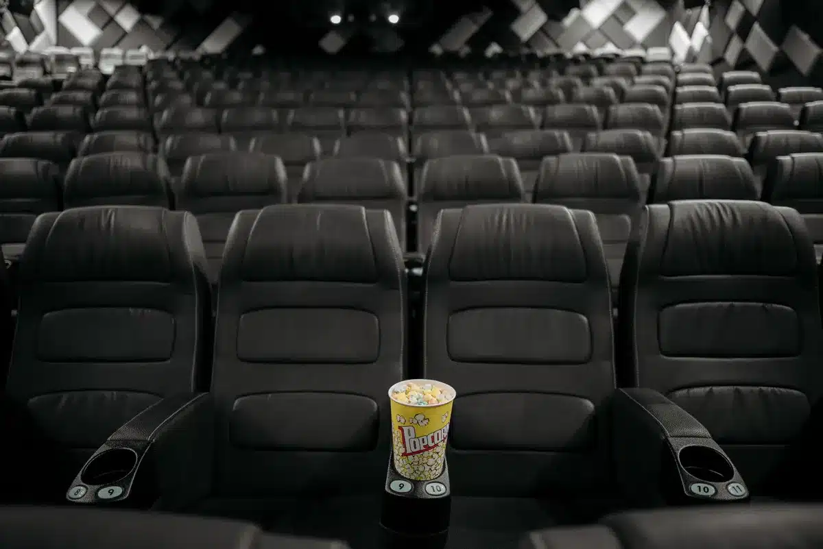A packed IMAX auditorium with the curved screen filling the field of view, audiences seated in reclining chairs, light from the massive screen illuminating faces in anticipation
