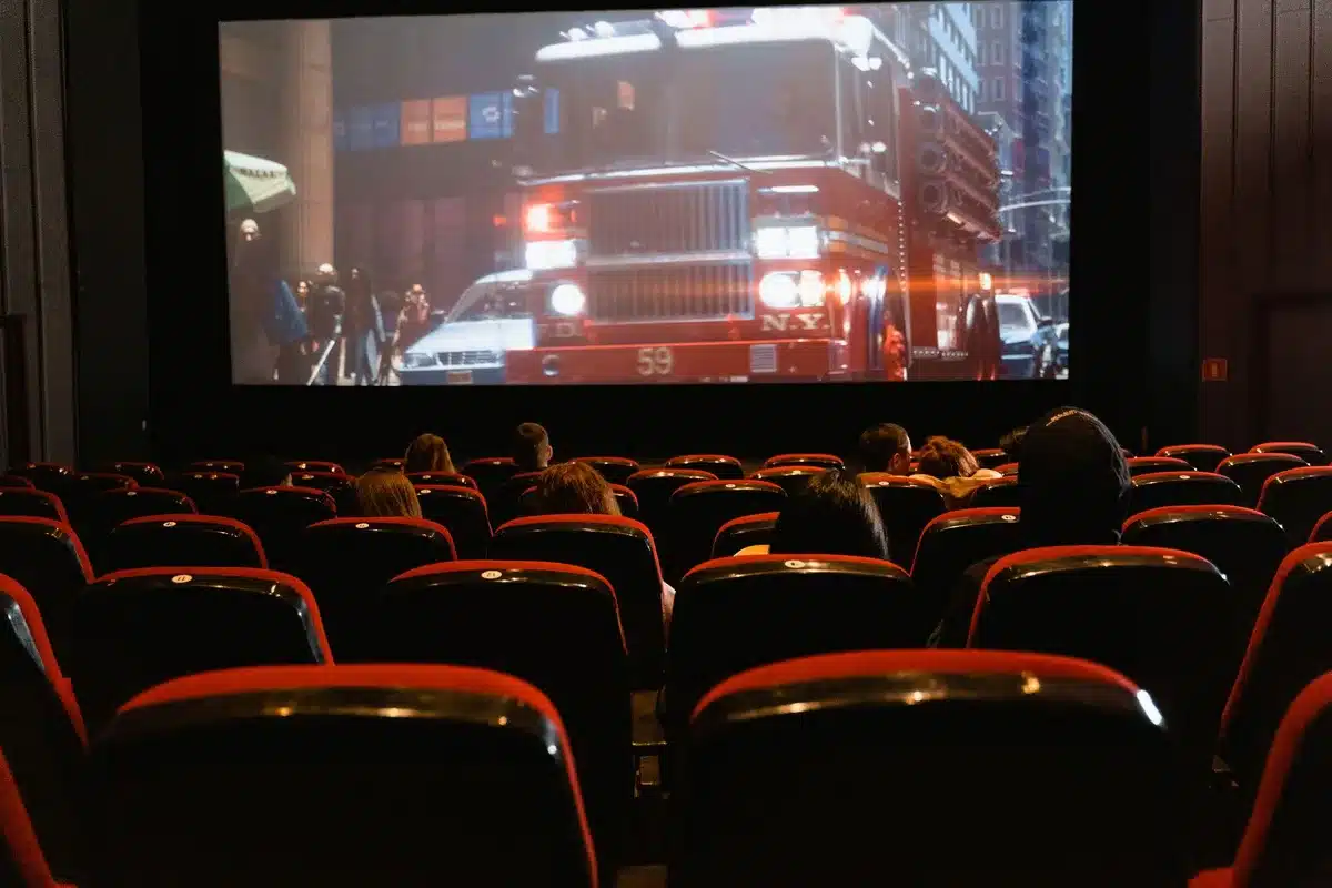 A theater auditorium filled with moviegoers seated in premium reclining chairs, watching a blockbuster film on a massive IMAX screen, the image capturing the scale and immersive quality of premium cinema