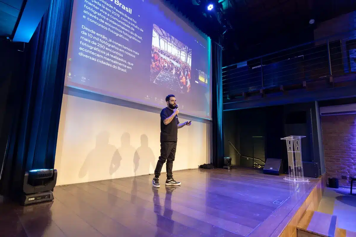 Conference stage with presentation screens displaying AI infrastructure diagrams and performance metrics, audience silhouettes in foreground