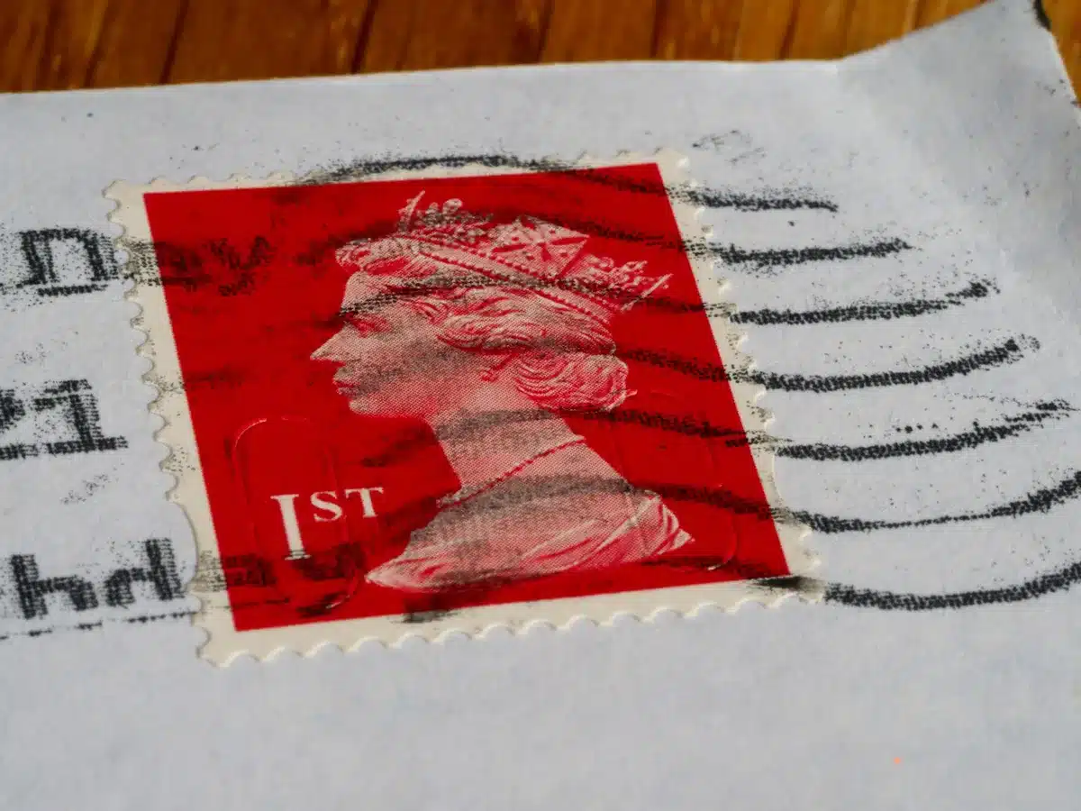 A stack of mail-in ballot envelopes with postal barcodes and official markings, arranged on a desk