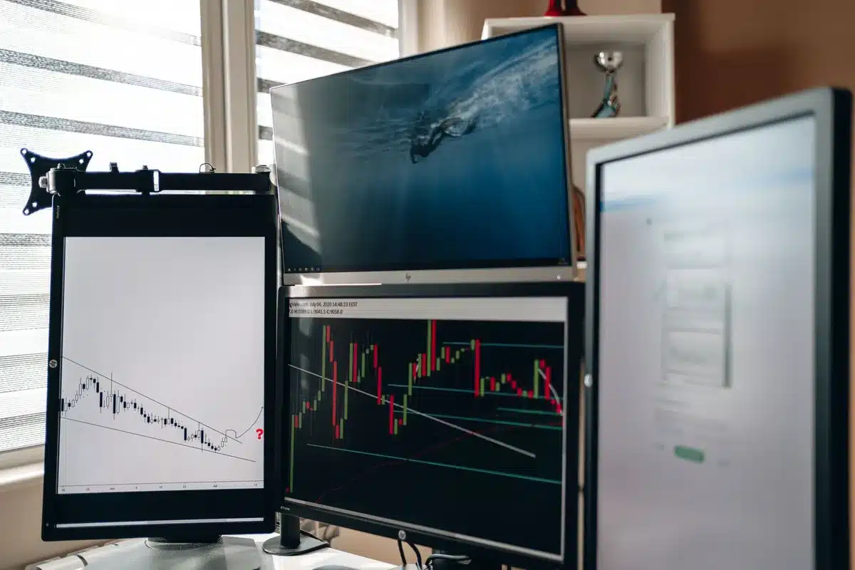 A pristine office space with multiple computer monitors displaying financial dashboards, one showing an ascending line chart in green and another in red, representing market competition.