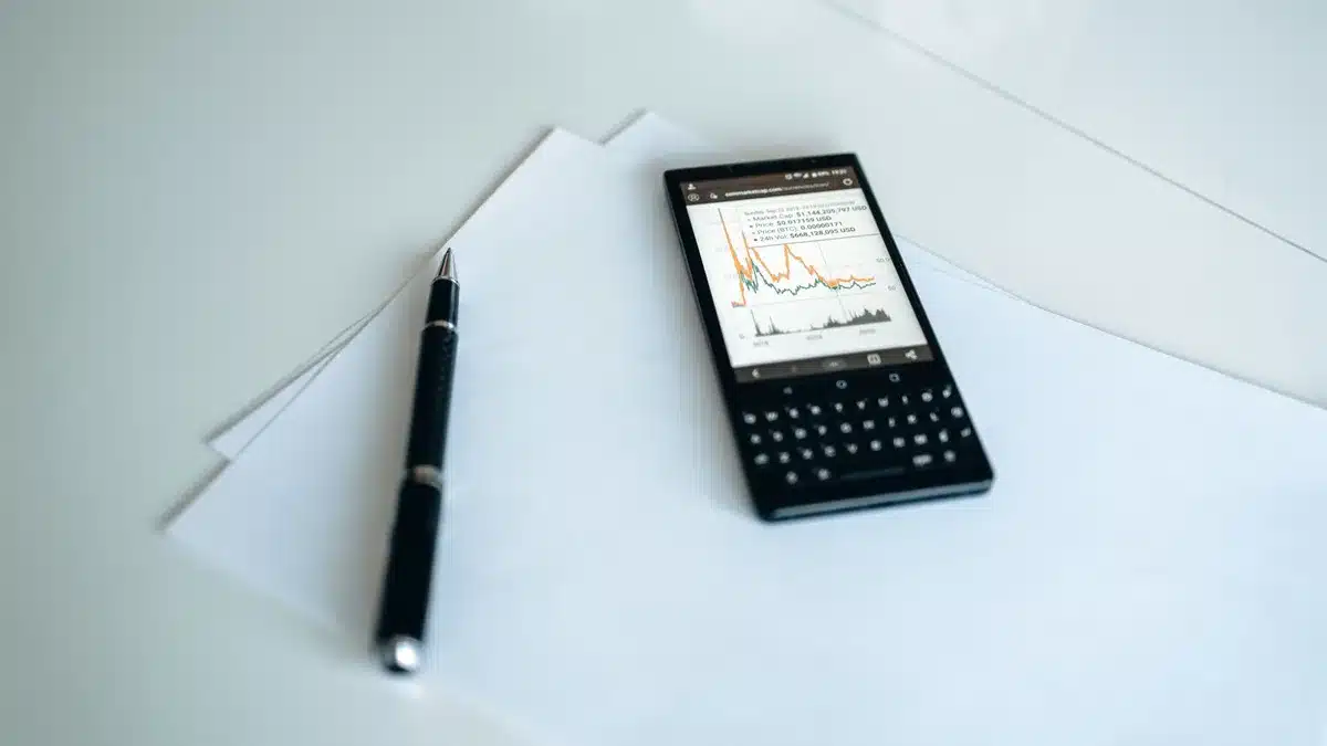 A sleek smartphone displaying financial data on its screen, surrounded by glowing stock ticker symbols and candlestick charts in warm amber light against a dark background, evoking market momentum and investor focus