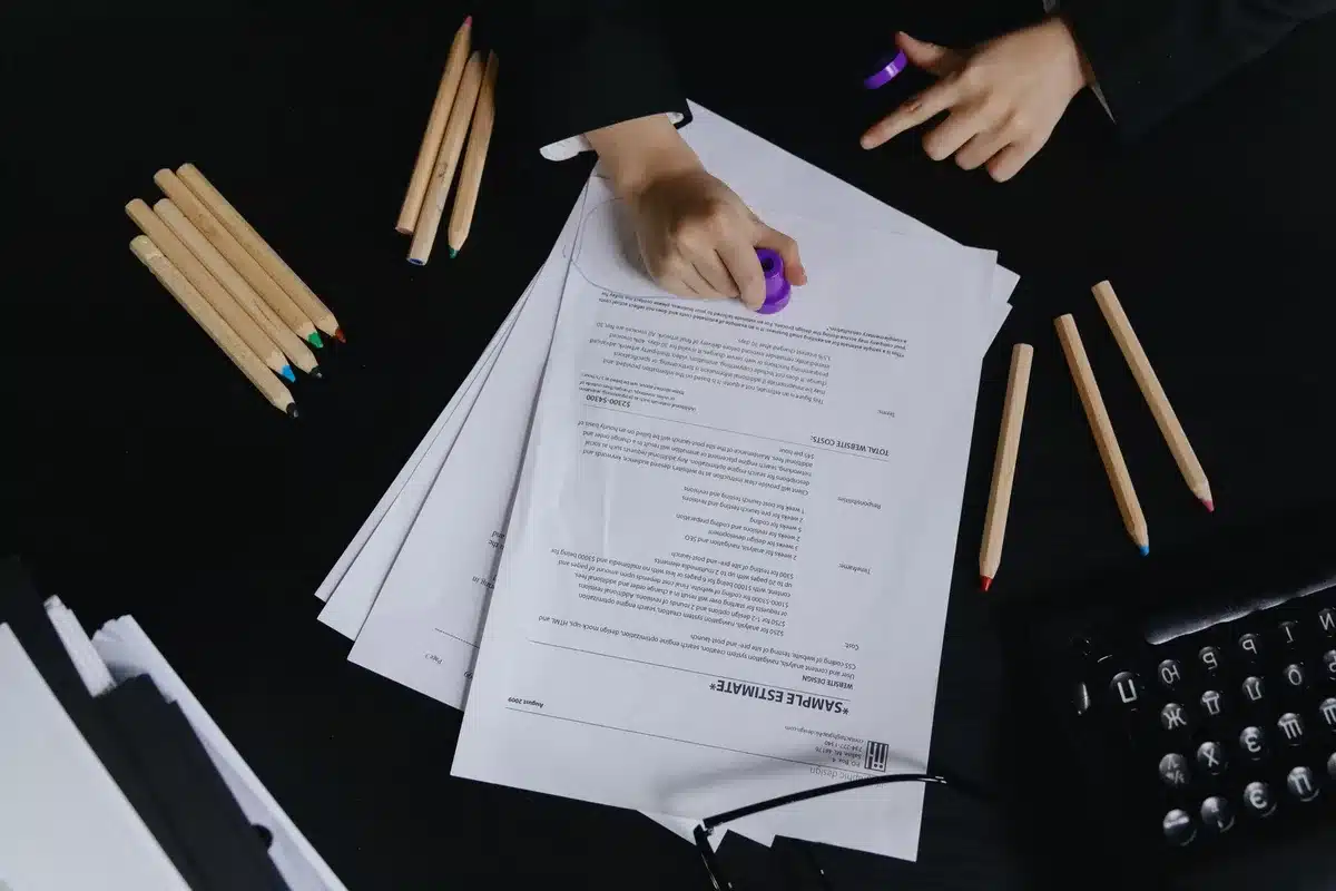 Stacks of redacted documents with black marker lines obscuring text, scattered papers on a desk, magnifying glass examining the redacted sections, official government letterhead visible