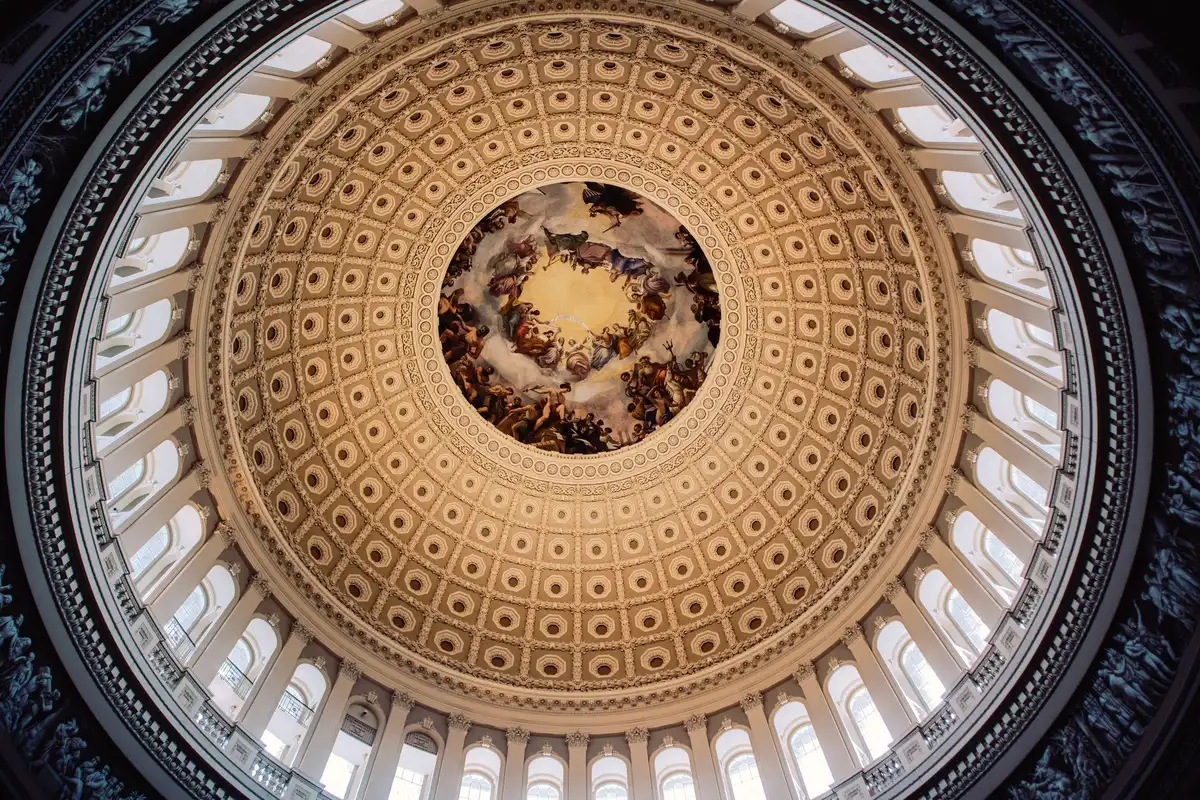 A formal Senate hearing room with empty seats and microphones, harsh overhead lighting casting shadows across wooden desks, a single gavel resting on the bench, the chamber quiet and still