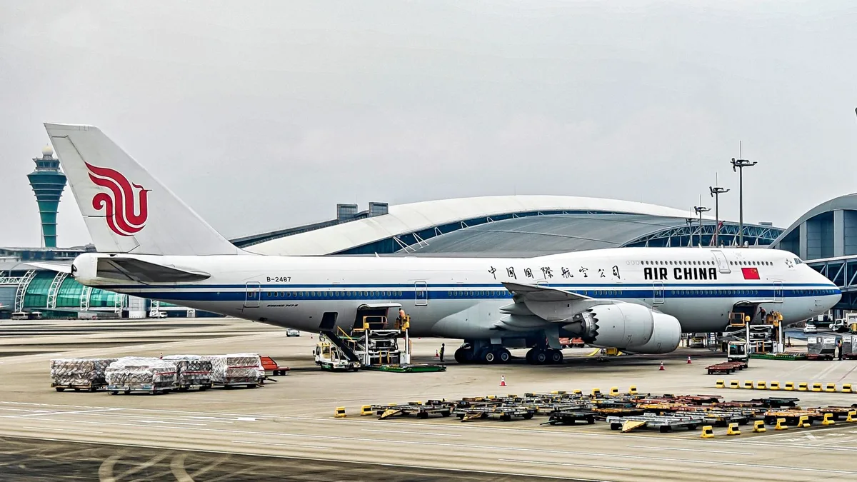 A sleek Boeing 747-8 aircraft parked on an airport tarmac in daylight, its distinctive fuselage visible from the side, with ground service equipment nearby and a clear blue sky above