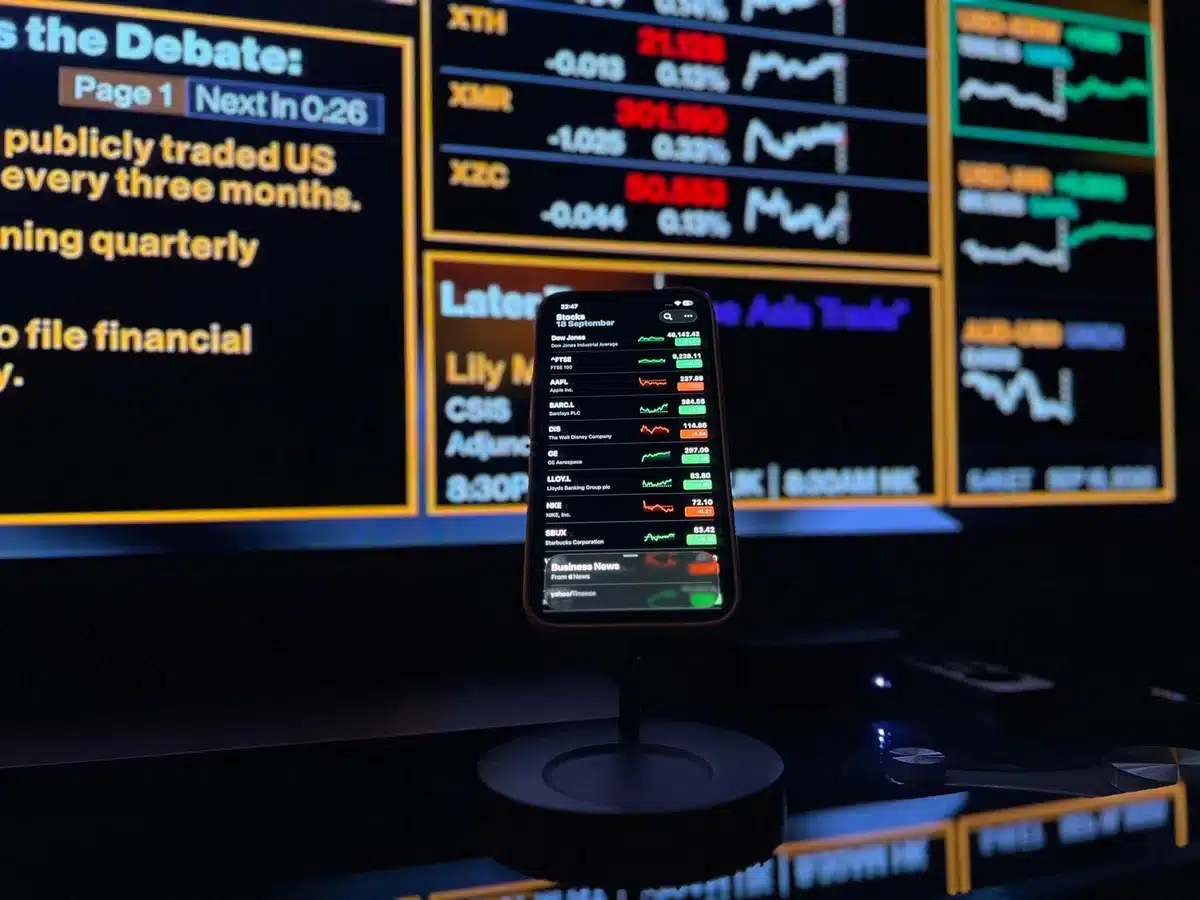 Stock market ticker display showing declining numbers in red, with abstract financial charts and candlestick patterns blurred in the background, representing market reaction