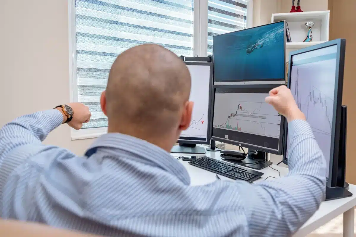 An anonymous investor silhouette facing multiple glowing screens displaying stock charts and market data, hands poised over a keyboard, cool blue and green light casting across the figure, determination and focus evident