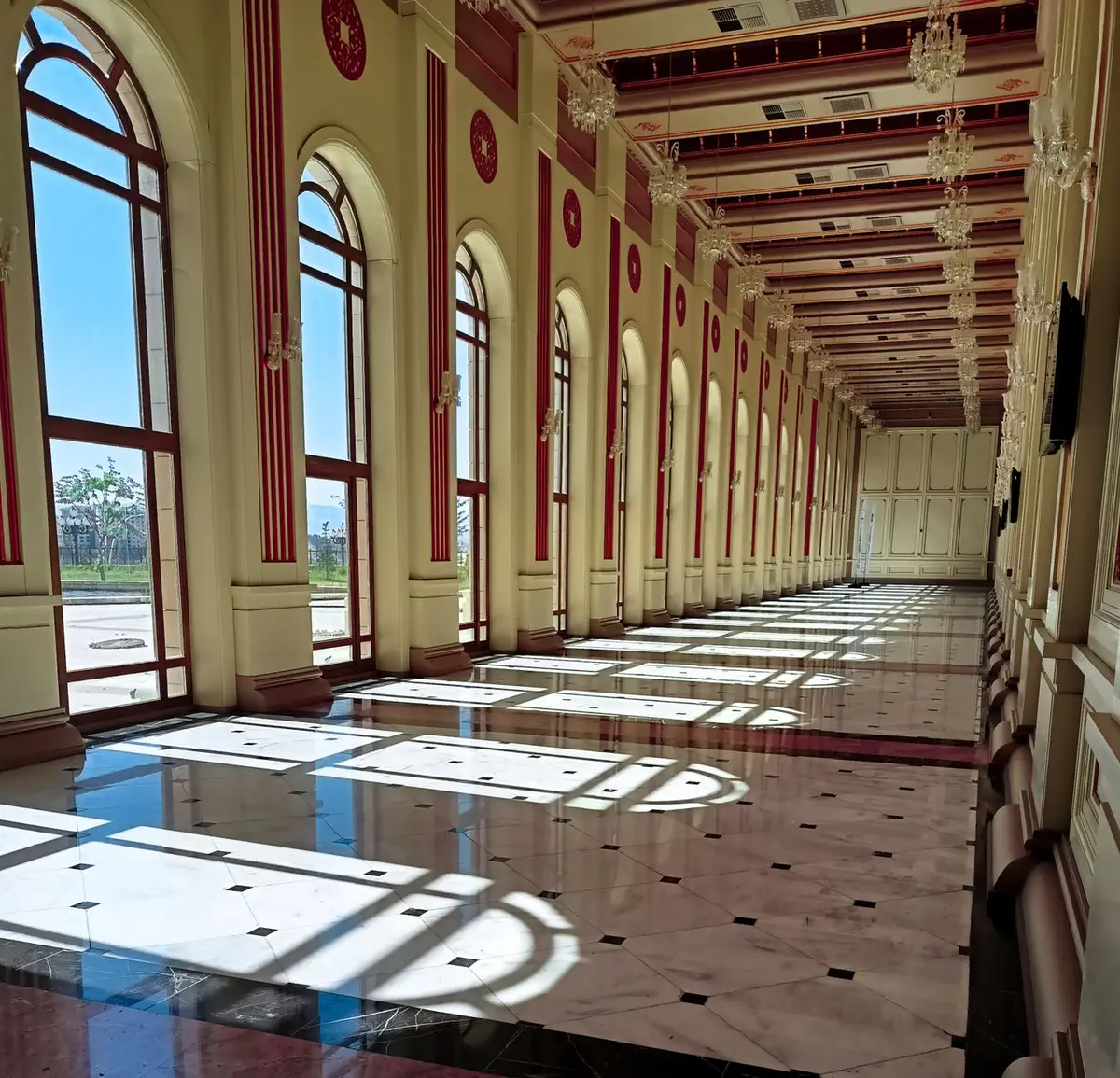 A formal palace corridor with ornate woodwork and soft natural light filtering through tall windows, an empty desk chair in the foreground, papers neatly arranged, suggesting institutional continuity and the weight of senior royal service