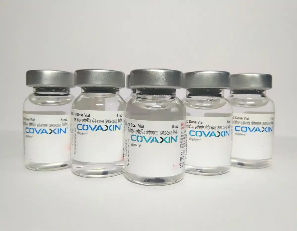 A vial of COVID-19 vaccine against a soft-focus background of medical equipment and a calendar showing autumn months, symbolizing seasonal vaccination readiness.