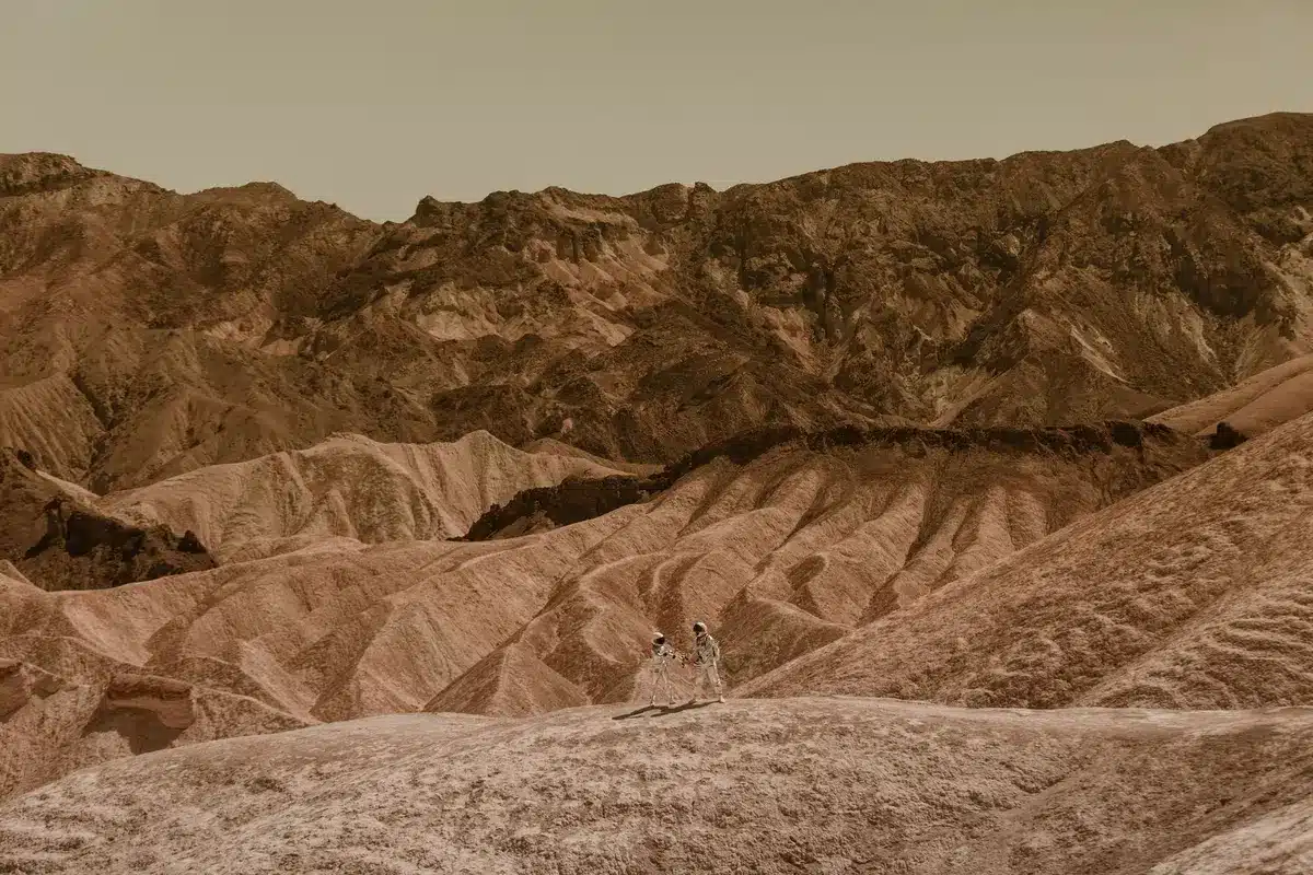A Martian landscape with scattered sharp rocks and uneven terrain showing the types of obstacles that damage rover wheels, with a distant ridge visible