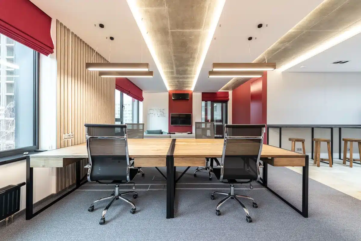 Two empty chairs facing each other in a dimly lit office, a desk between them, one bathed in warmer light and one in cooler shadow, creating a visual tension between the two positions