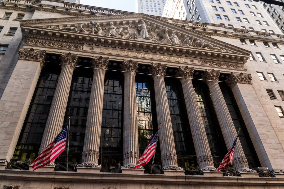 A crowded trading floor with traders monitoring multiple screens displaying real-time stock prices and earnings charts, phones in hand, focused expressions