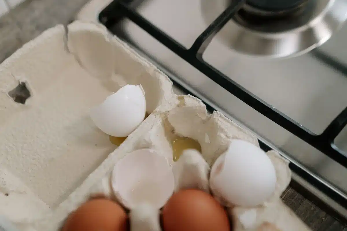 Cartons of white and brown eggs on grocery store shelves, with product codes and date stamps visible on the sides of packaging, neutral lighting