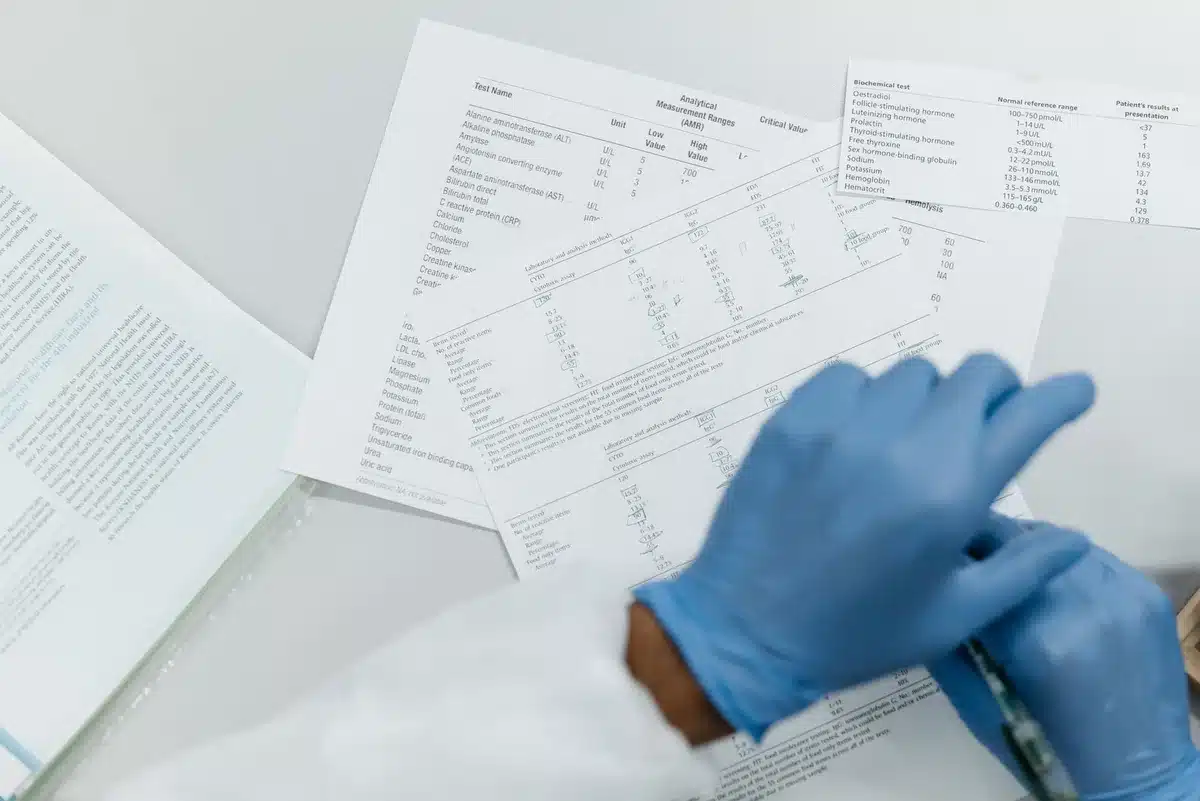 A healthcare worker in gloves handling laboratory samples in a clinical setting, microscope and test tubes visible, blue-tinted lighting