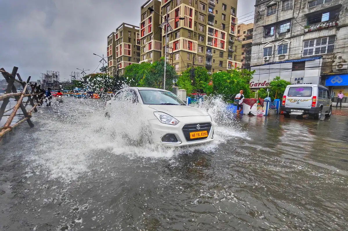 Flooded residential street with water submerging parked vehicles and mailboxes, heavy rain falling, dark storm clouds overhead, a single palm tree bending in wind
