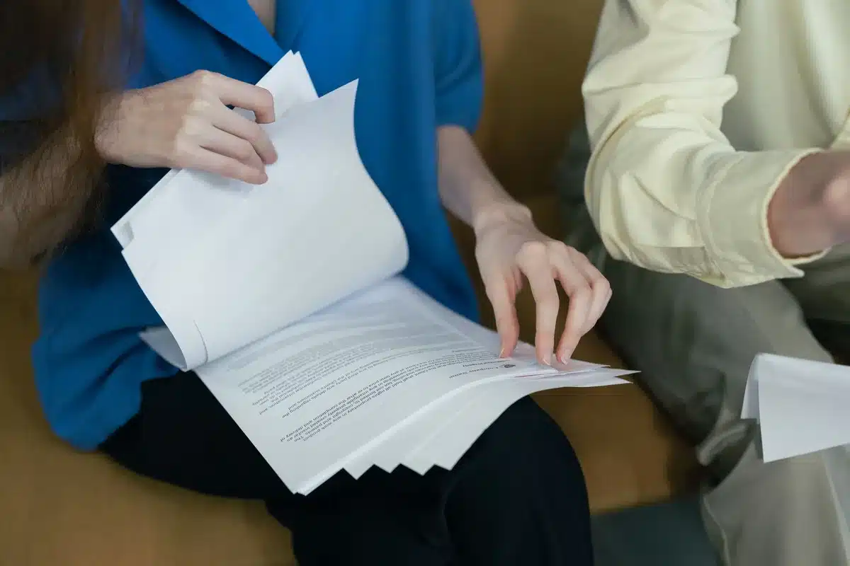 A desk covered with scientific papers, peer-reviewed journals, and research documents with highlighted sections, a magnifying glass resting on one page, soft natural light illuminating the materials, suggesting careful scientific scrutiny.