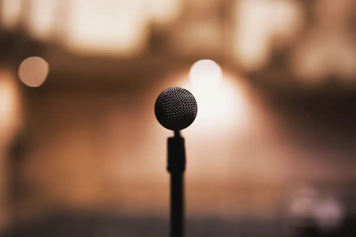 Late-night talk show set with empty host chair and guest seat under studio lights, microphone visible, a stark minimalist stage