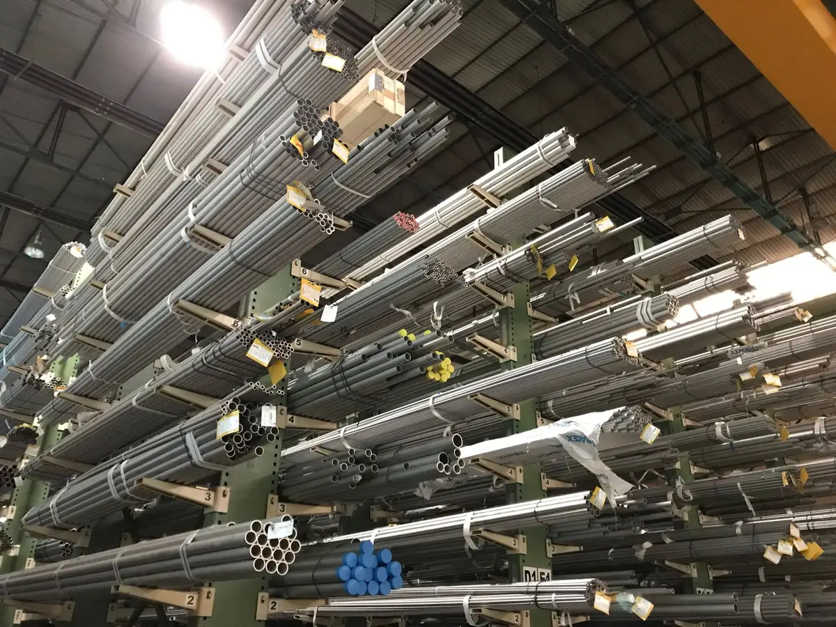 Aluminum coil stock in industrial warehouse setting with stacked inventory, industrial lighting, neutral gray tones emphasizing material supply and logistics