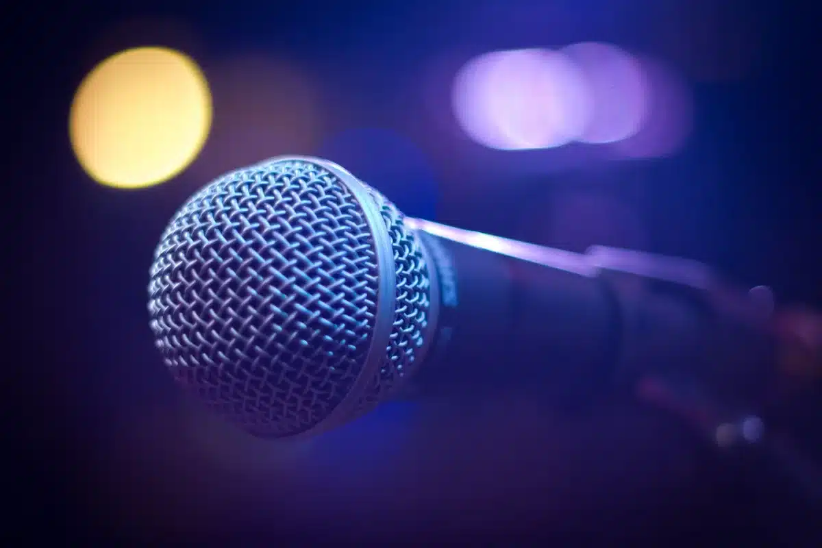 A studio microphone on a stark, empty debate stage under a single spotlight, shadows stretching across empty seats, tension and confrontation implied