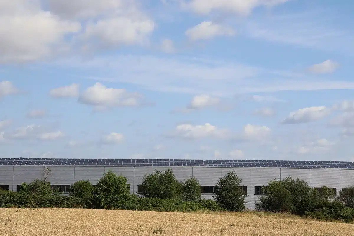 A wide shot of an industrial data center facility exterior at dusk, with illuminated windows and a glowing power infrastructure, renewable energy panels visible on the roof, emphasizing the scale of the operation.