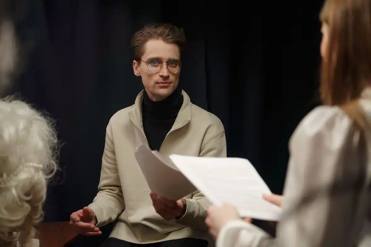 A young man in a recording studio, headphones around his neck, studying sheet music under warm studio lighting, focused and determined.