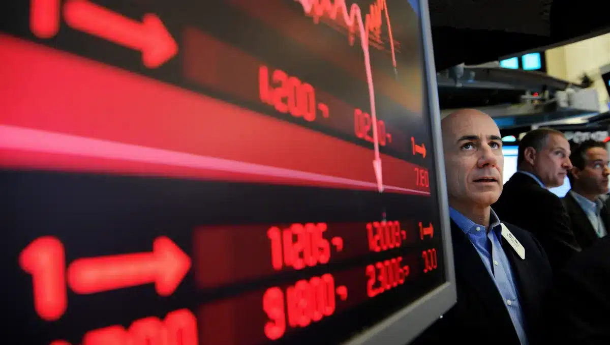 A stock trading floor screen displaying declining Jersey Mike's shares, with red numbers and downward arrows, traders in the background watching the opening bell ceremony | stock market display