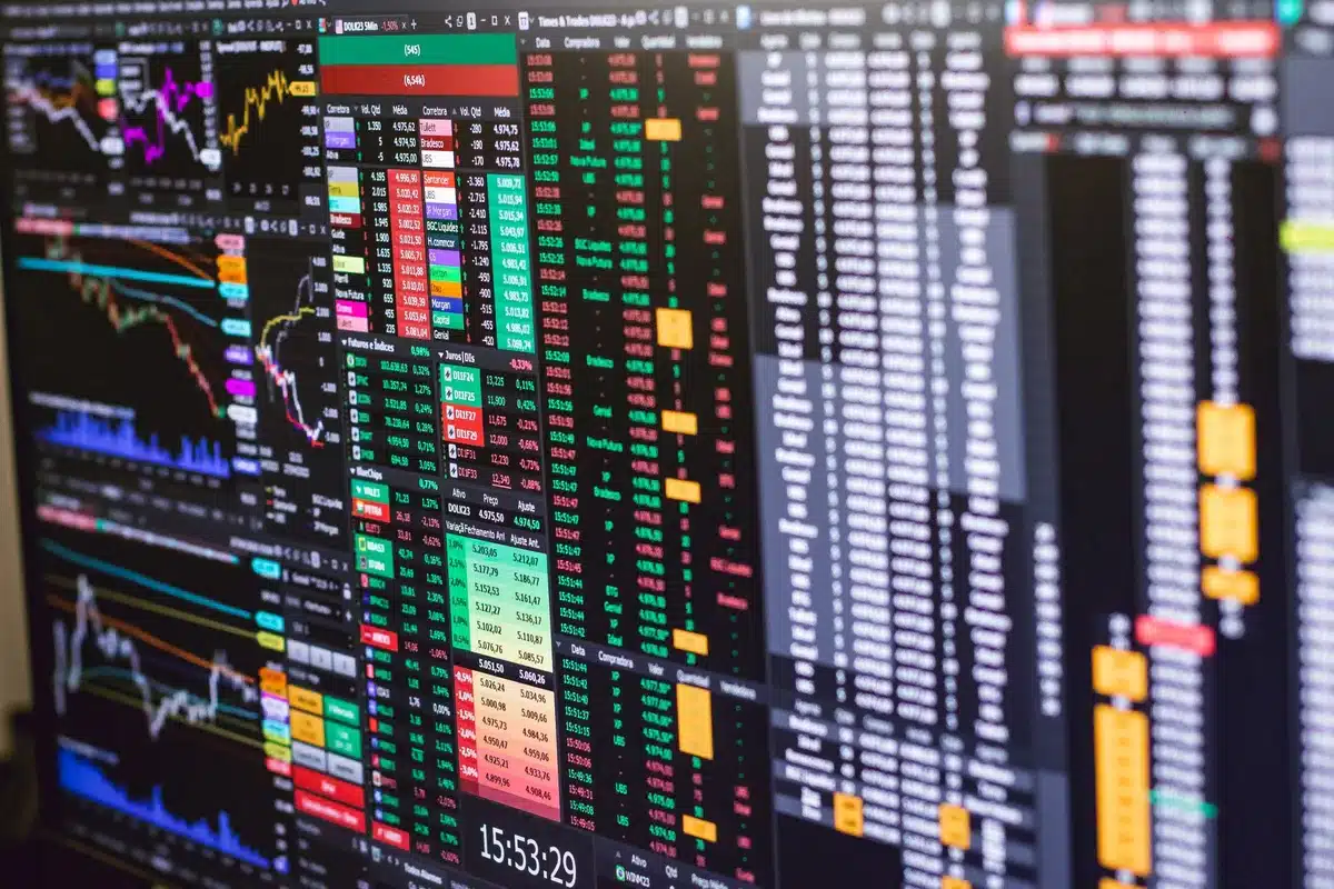 Blurred stock market screens displaying red numbers and declining charts, a trading floor in shadow, anonymous traders at desks, tension in motion