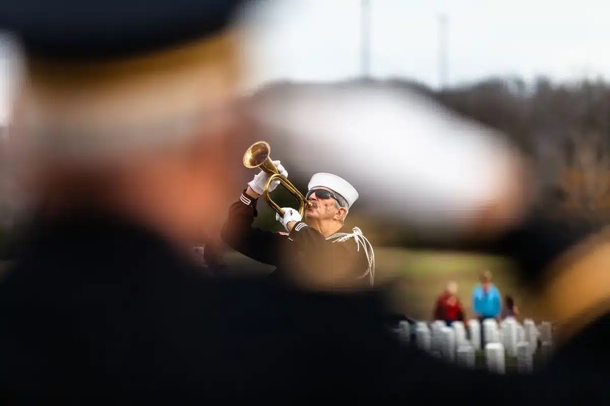 A solemn Capitol Rotunda with military honor guard standing at attention beside a flag-draped casket, soft morning light filtering through the dome, wreaths of flowers at the base, the weight of state ceremony in stillness