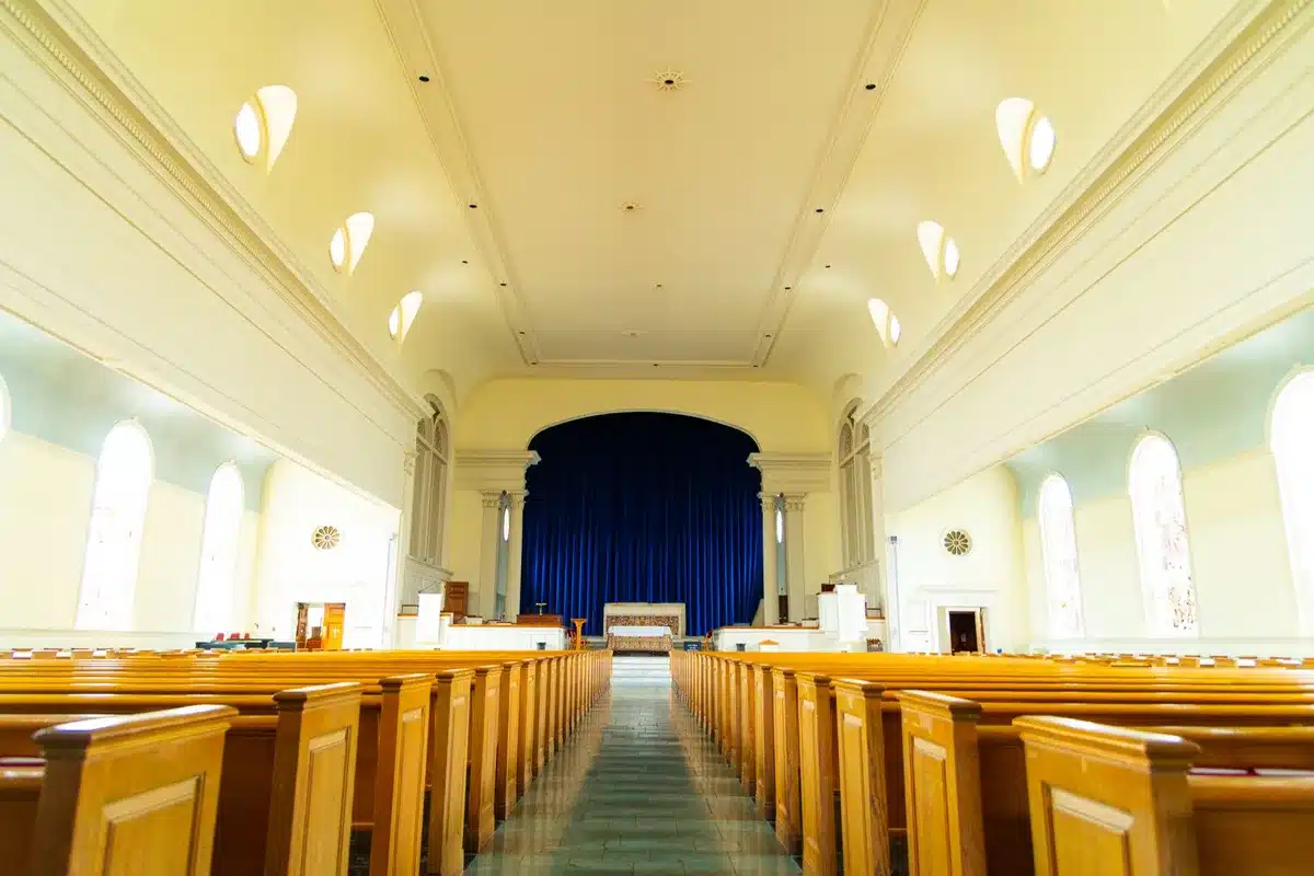An empty sanctuary with wooden pews and a simple pulpit, soft light filtering through stained glass, a single hymnal resting on a bench