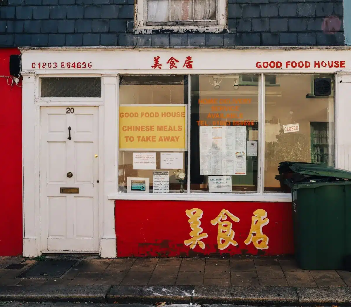 A quick-service seafood restaurant storefront with a weathered facade and closed signage, empty parking lot under overcast sky, mid-afternoon light casting long shadows across the pavement.