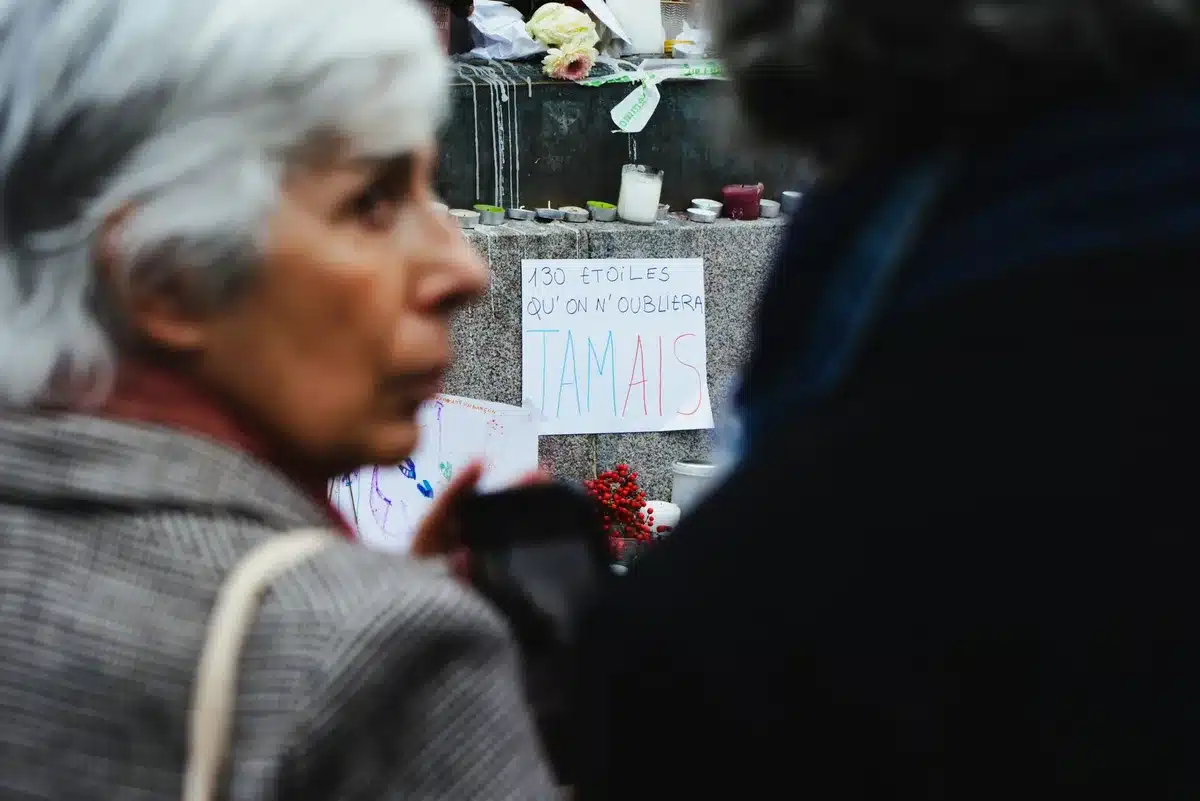 A grieving figure standing alone before an inscribed name on the memorial wall, hands pressed against the stone, morning light diffusing through mist, the figure's silhouette framed by the vast plaza