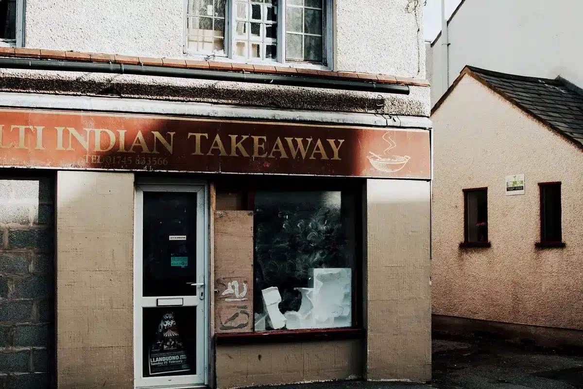 An empty restaurant storefront with closed signage visible, fluorescent lighting reflecting off darkened windows, and a vacant interior space.