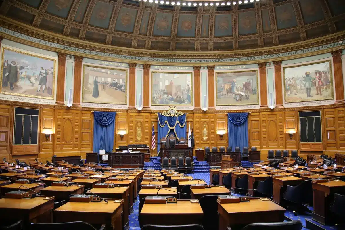 A senator's empty desk in a chamber with rows of vacant seats, soft light filtering through tall windows, a gavel resting on mahogany, the weight of absence