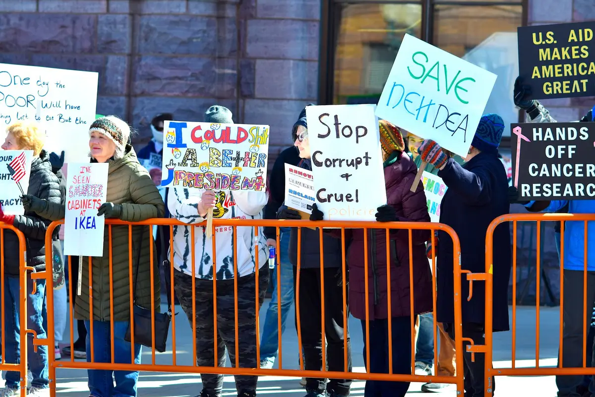 A diverse crowd of supporters gathered at a Democratic rally in Detroit, holding campaign signs and flags, faces animated with engagement, a sense of grassroots momentum in the air.