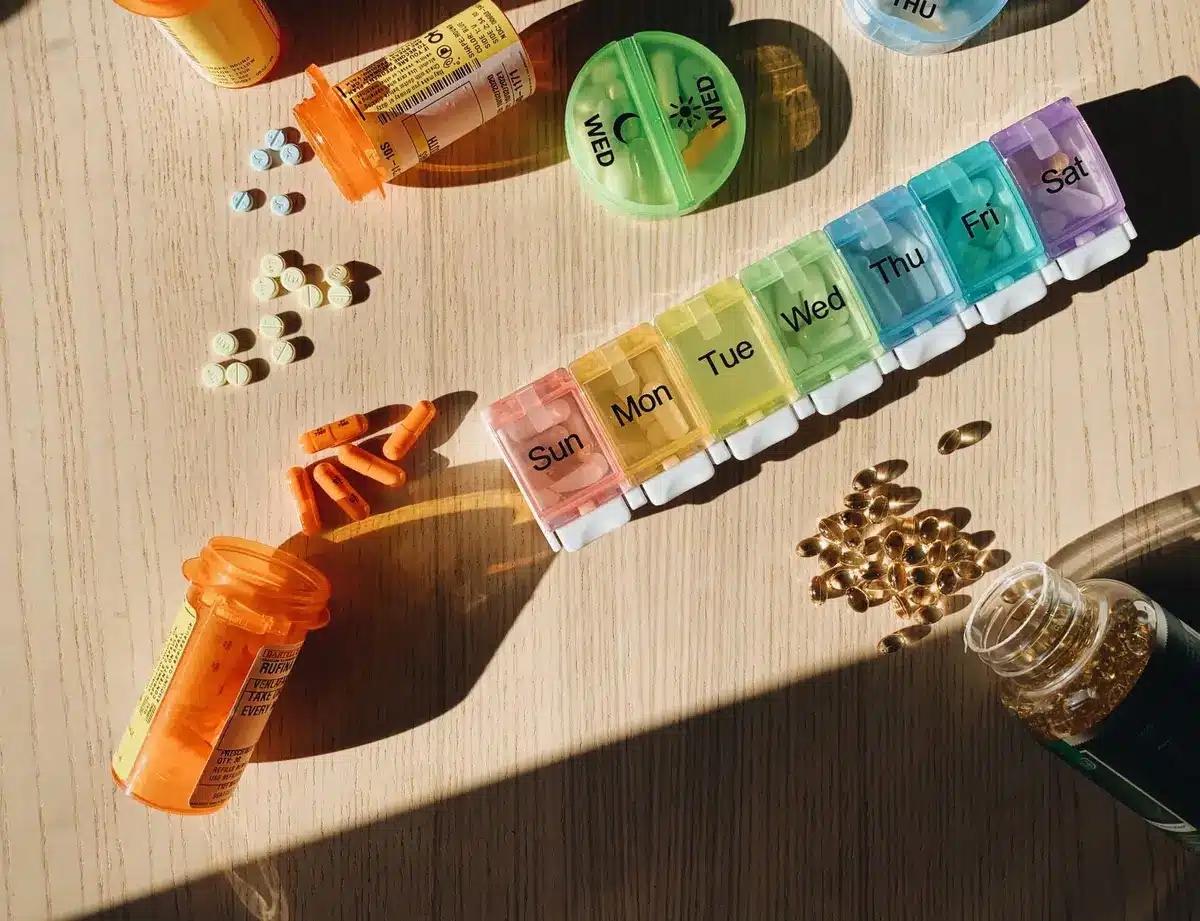 Prescription medication bottles and pills arranged on a pharmacy shelf, with a pharmacist's blurred hand reaching for a container, soft pharmacy lighting in the background