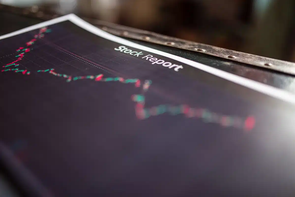 Glowing stock market ticker displaying red numbers and downward arrows, dim trading floor background, anonymous traders in silhouette watching screens