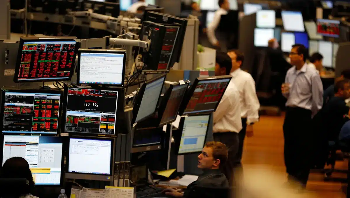 Busy trading floor with multiple monitors displaying stock indices and currency rates, red numbers dominating the screens, traders in focus blurred in background | semiconductor trading floor
