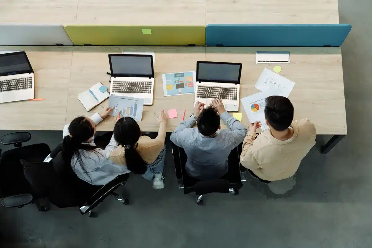A corporate office with employees working at computers, with a glowing AI interface overlay on screens, showing the tension between productivity tools and escalating costs