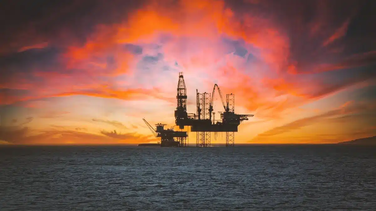 Oil production platform in Nigerian waters with workers monitoring operations, crude being extracted and loaded, clear daylight showing offshore infrastructure against calm waters
