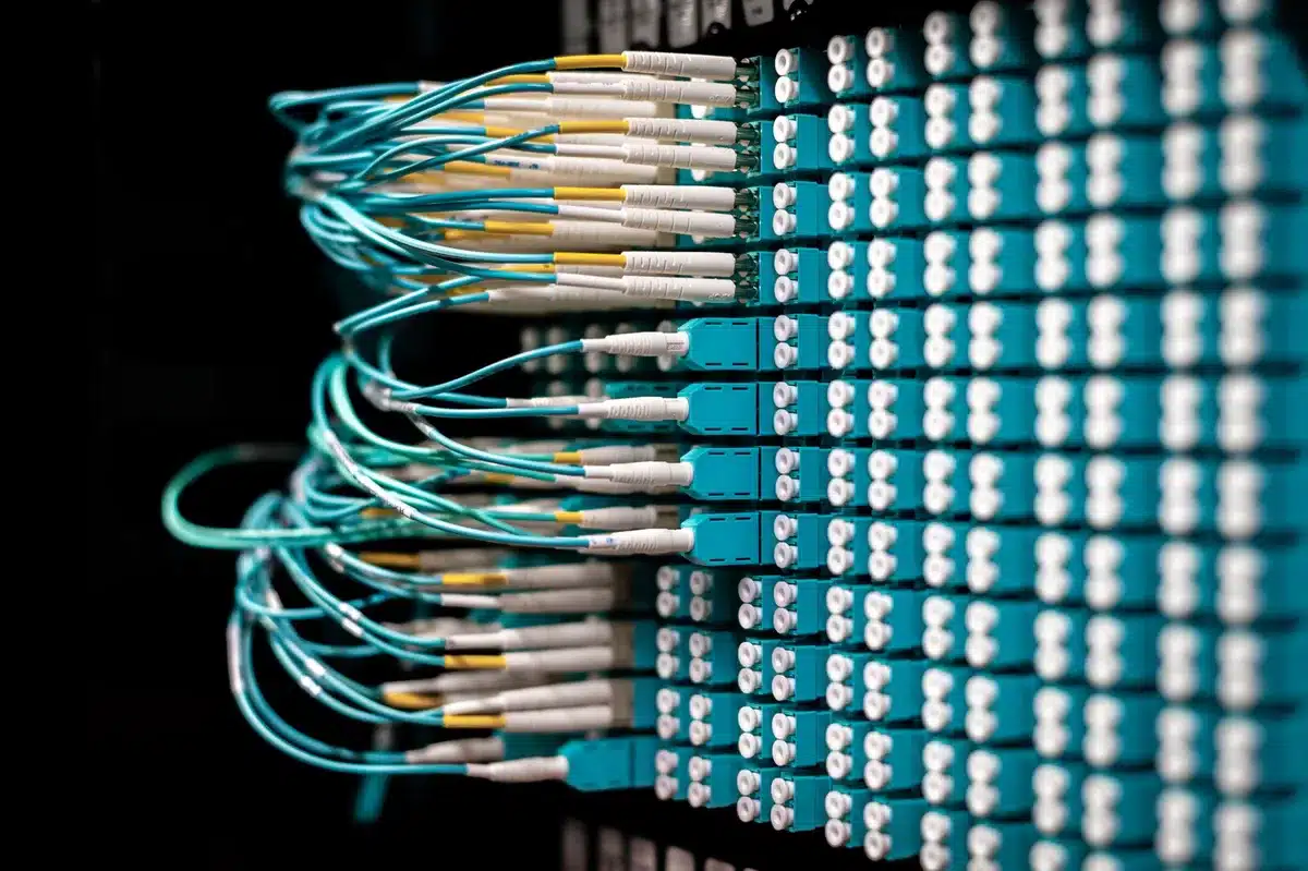 A data center server room with rows of computing equipment and cooling systems, bathed in blue and white light, representing the massive power demands of AI infrastructure.
