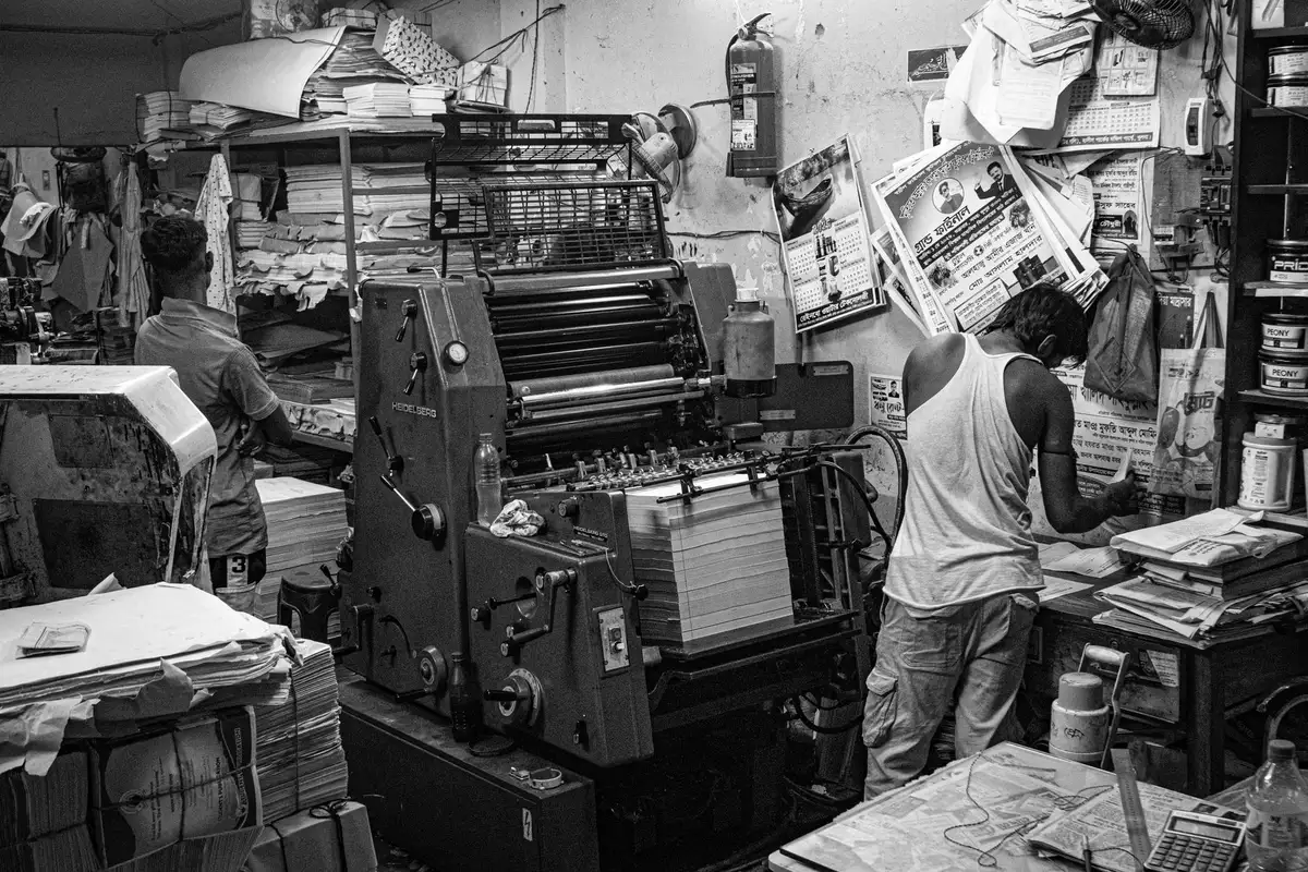 Newspaper printing press in motion with blurred pages flowing through, bold headlines visible, warm amber light on metal machinery, symbolizing journalism's resilience