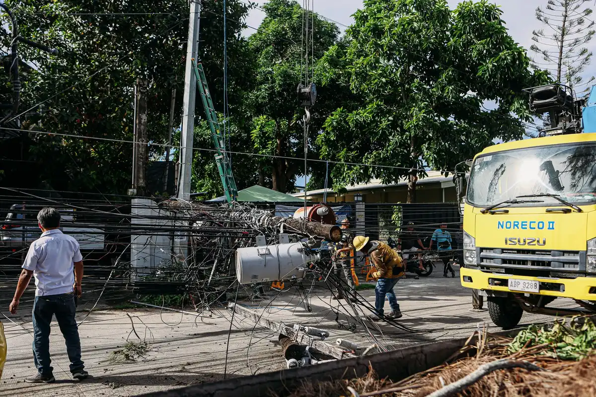 Utility poles snapped and toppled by extreme winds, lying across roads and debris scattered in a residential area, storm clouds clearing overhead.