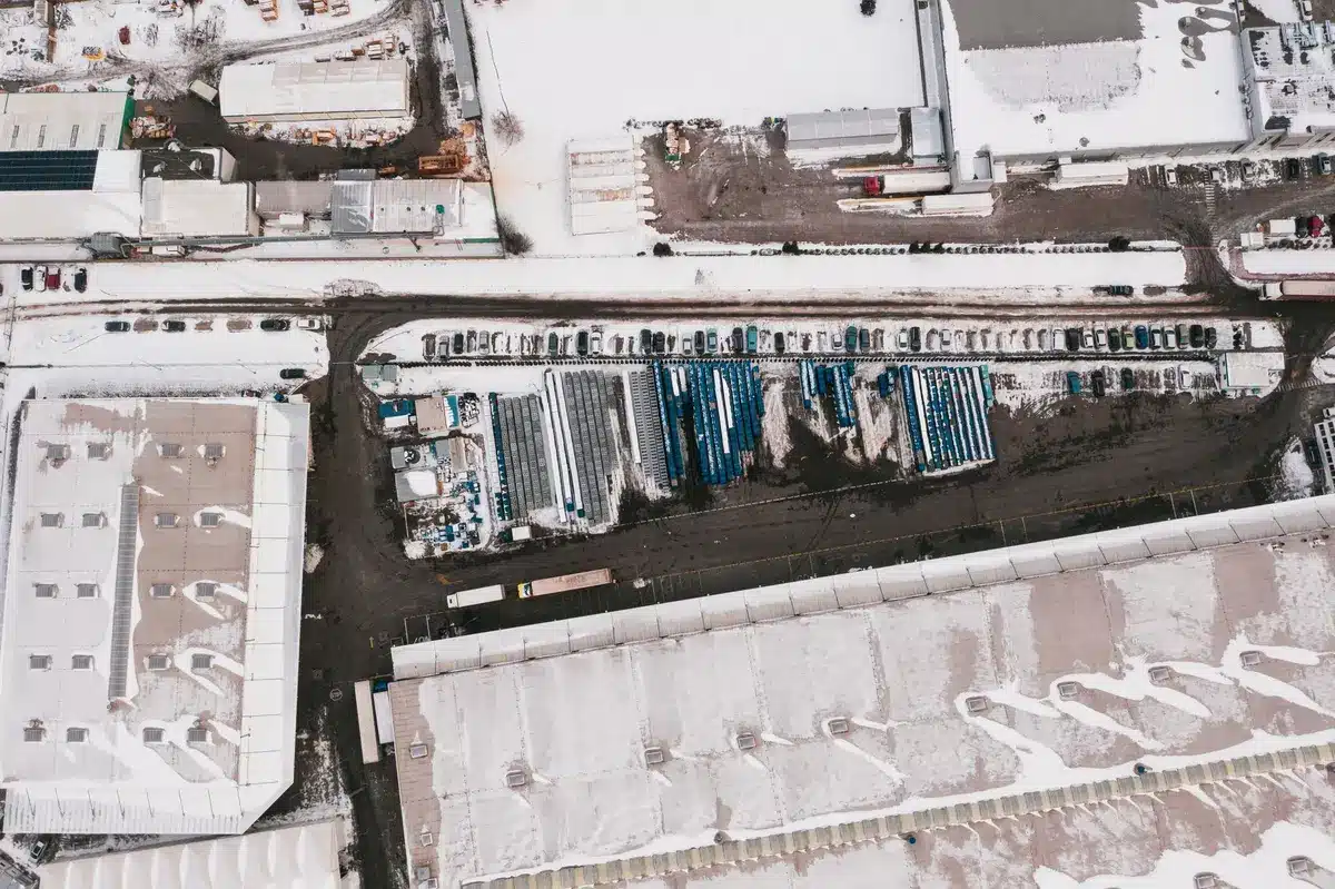 Aerial view of sprawling data center campus with rows of server buildings and cooling towers in a Virginia industrial park, surrounded by empty parking lots and transmission lines stretching to the horizon