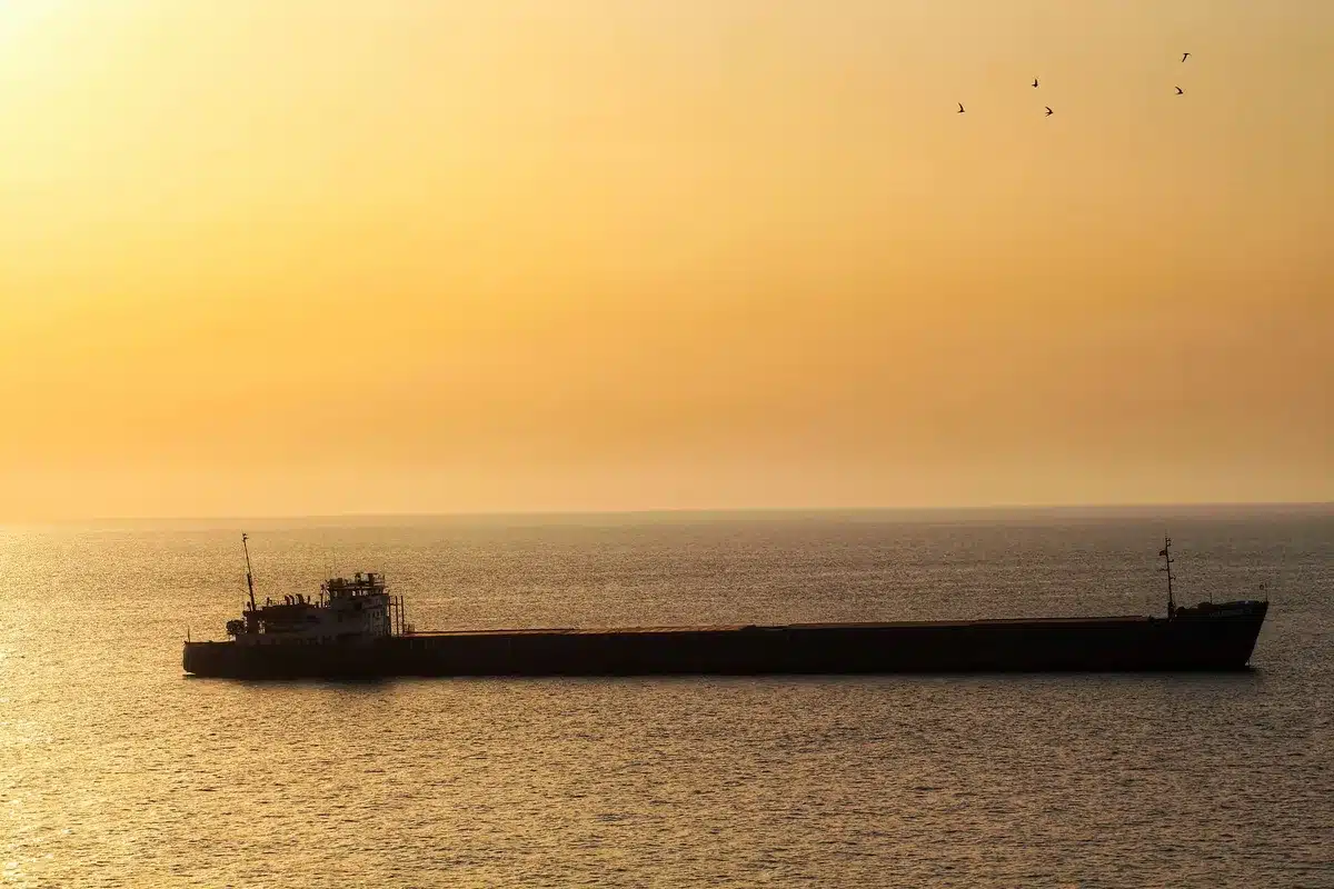 Oil tanker ship navigating through narrow strait with military vessels visible in distance, tension in the waters