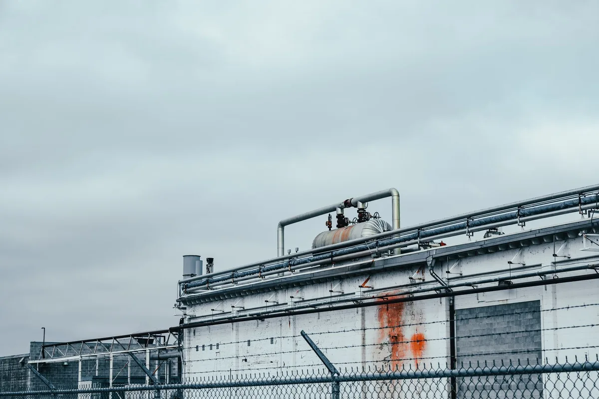 A modern industrial facility under construction with quantum technology logos and manufacturing equipment visible, representing the future FaQtory supplier building.