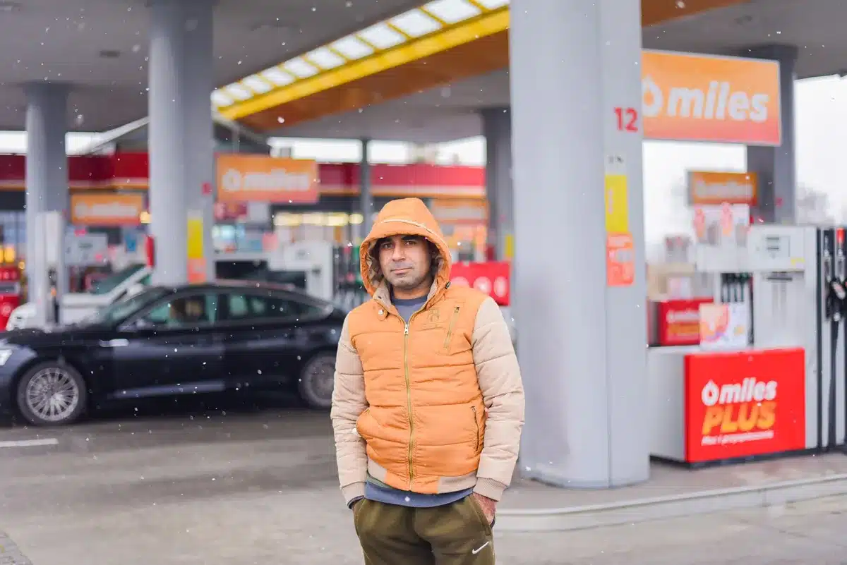 Long lines of cars at a Russian gas station, drivers waiting hours to refuel, visible frustration and fatigue on faces, daylight fading into dusk, a crowded pump area with empty tanks and limited availability visible