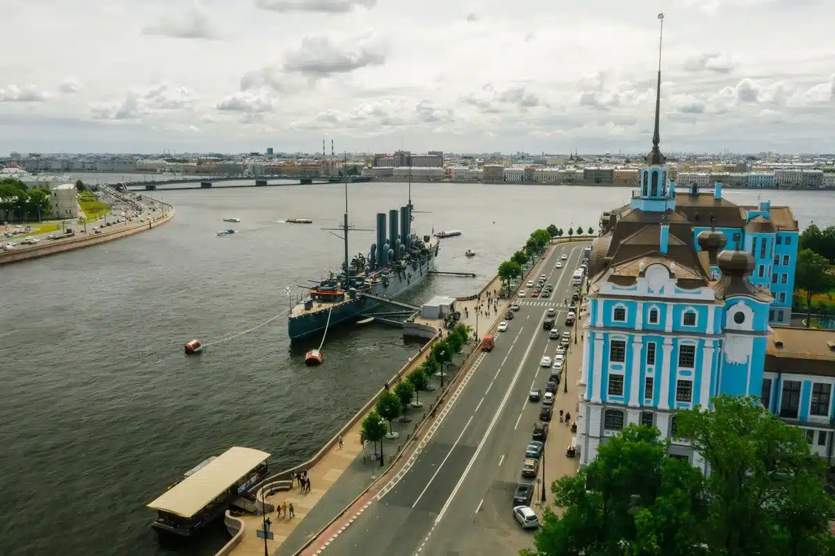 Military parade ground in St. Petersburg with naval vessels visible in the distance, empty reviewing stands, overcast sky