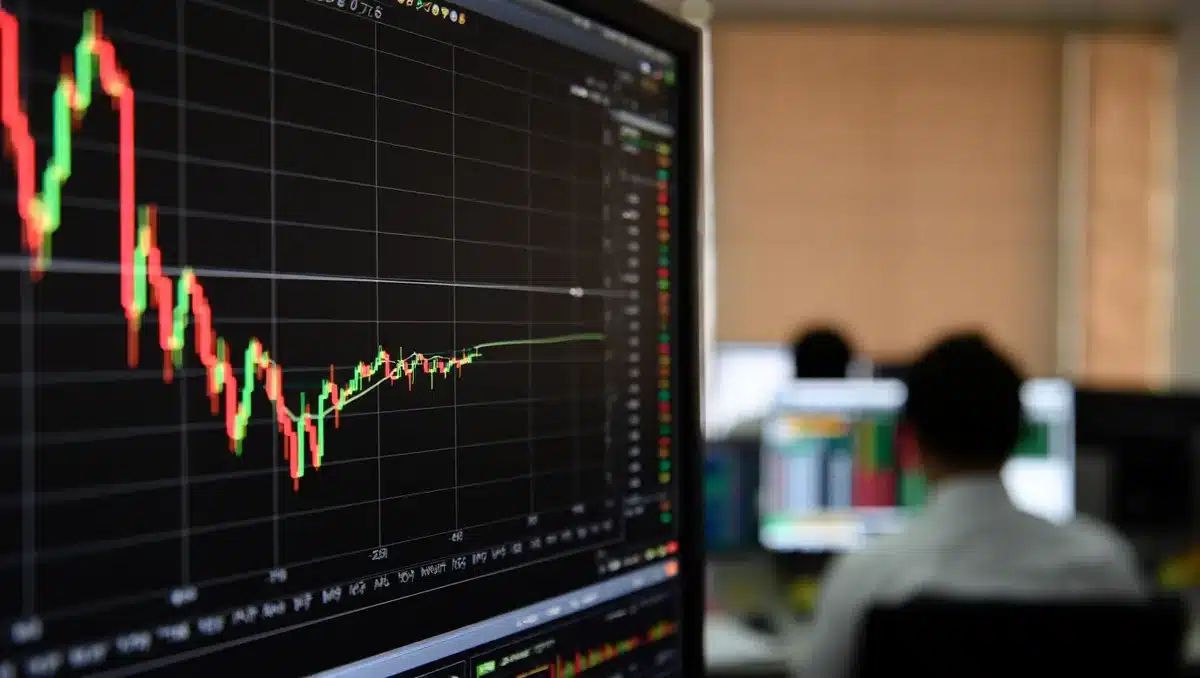 A stock market trading screen showing red and green candlestick charts with financial data, a blurred office environment in the background | stock market volatility screen