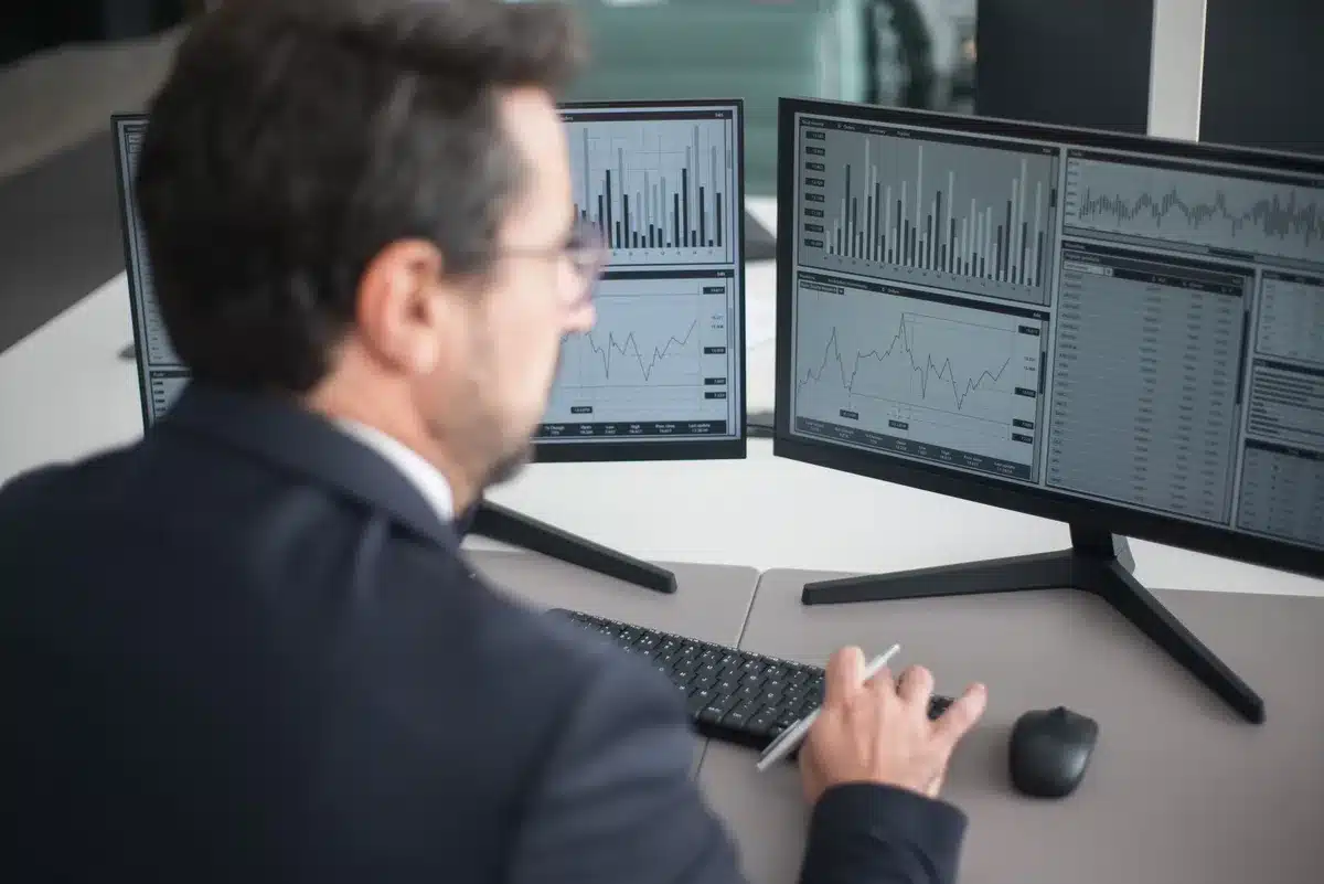 A silhouette of a person at a computer, staring at a glowing screen displaying stock charts and financial data, with a clock showing late evening hours.
